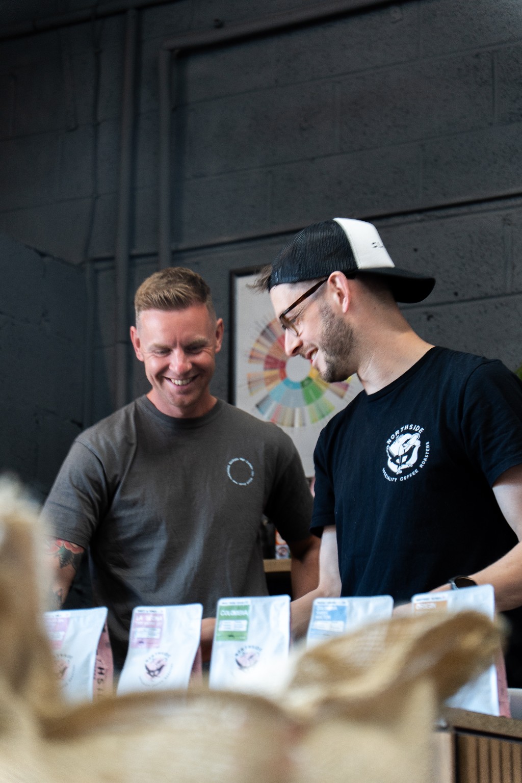 Two people smiling together beside bags of Northside coffee at the roastery
